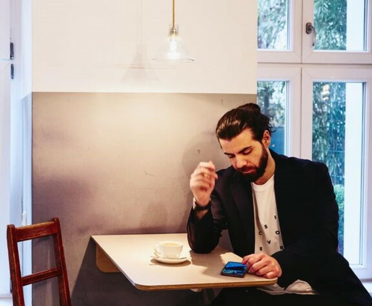 Man sitting at table with a coffee, looking seriously at his phone.