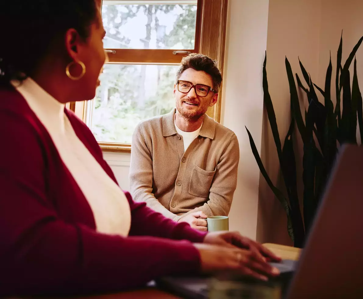 Female behind her laptop talking to male next to her at home