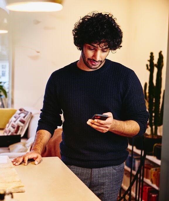 Man standing next to the kitchen counter top, looking at his phone.